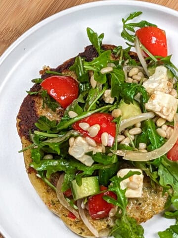 Golden-brown omelet topped with arugula, feta, tomatoes, and sunflower seeds on a white plate.